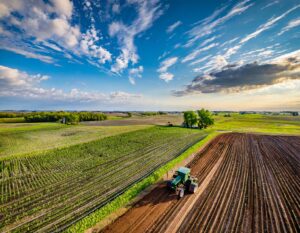 Tractor tilling rich, dark soil in a vast field, aerial perspective.
