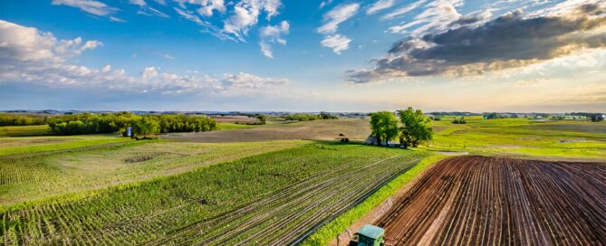 Tractor tilling rich, dark soil in a vast field, aerial perspective.